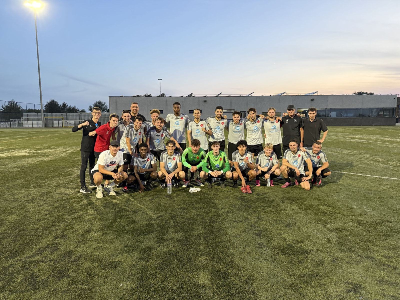 De ploeg van Merchtem United samen op het veld na de wedstrijd, bij zonsondergang.